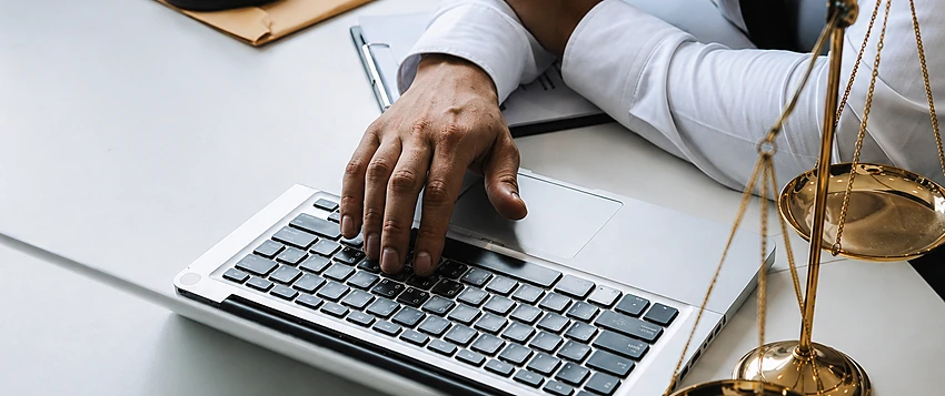 Legal professional conducting online research with scales of justice and a gavel on the desk